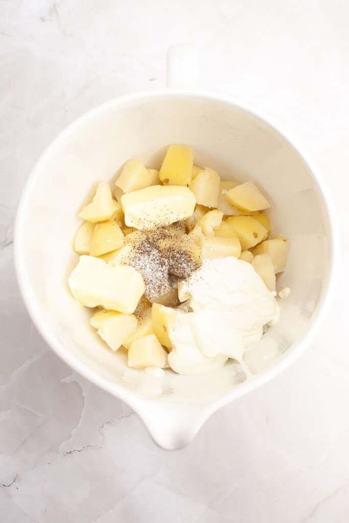 Potatoes, butter, and seasonings in a large bowl.