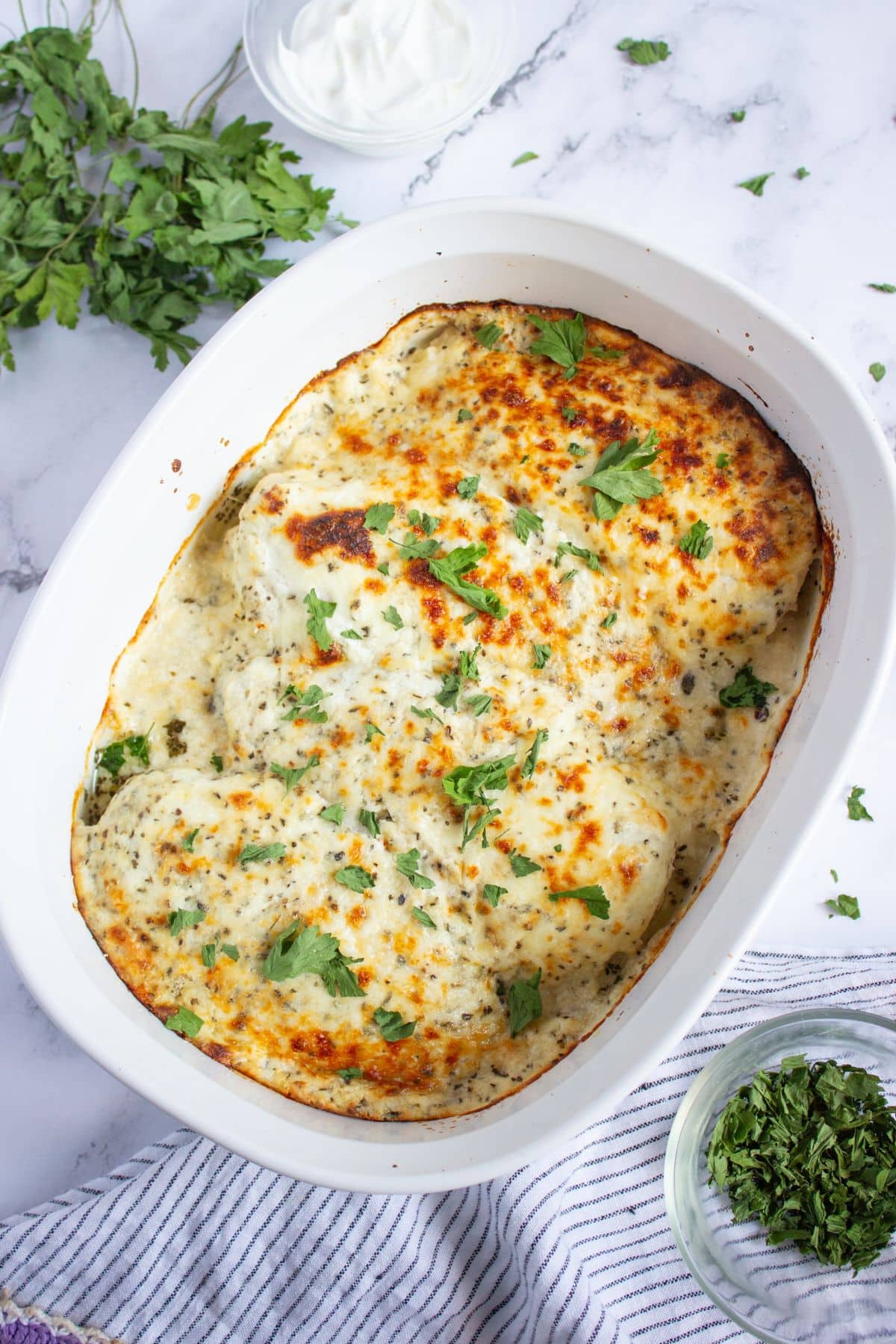 A white baking dish filled with baked cheesy sour cream chicken, golden brown on top with specks of herbs