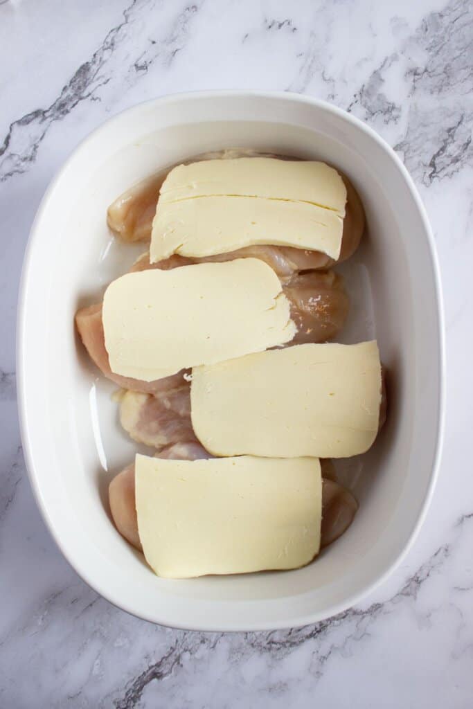 Cheese sliced being put on top of meat in a casserole dish.