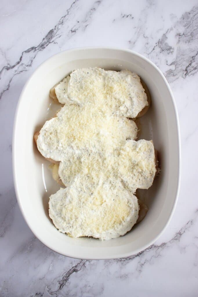Cheese being sprinkled on top of meat in a casserole dish.