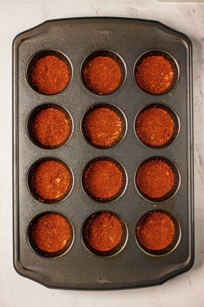 Crust being pressed into a muffin pan.