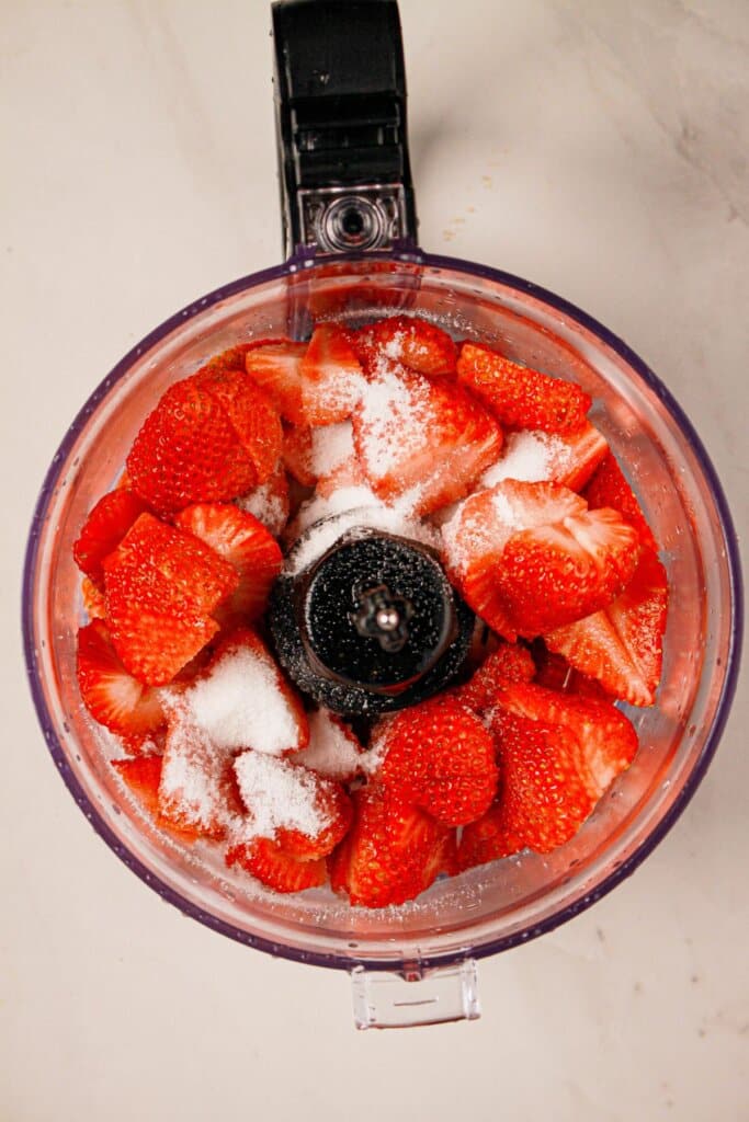 Strawberries and sugar in a food processor.