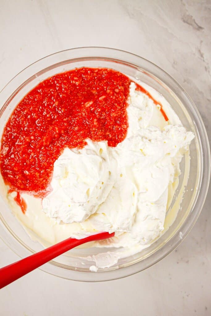 Fruit puree being mixed into whipped cream in a glass bowl.