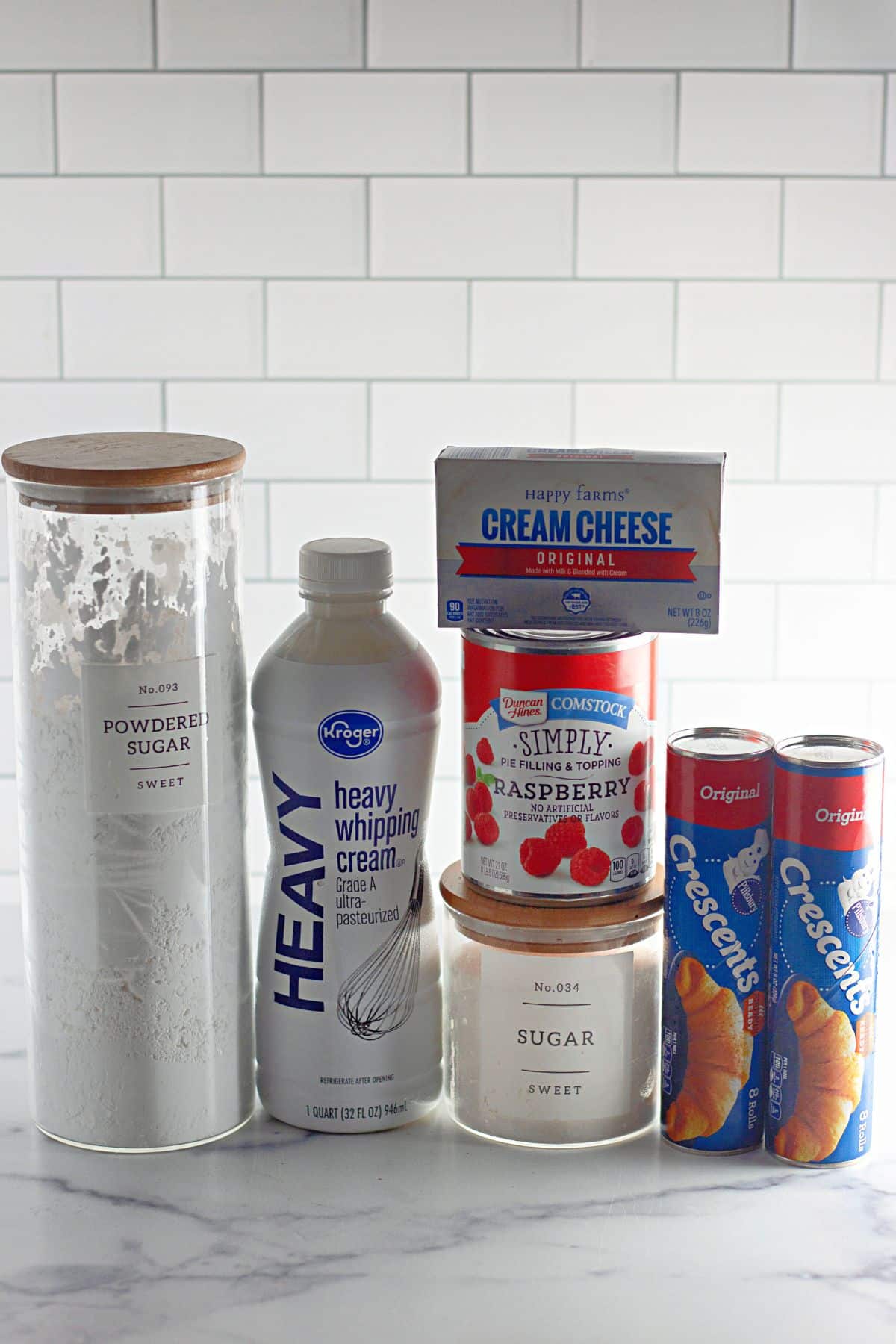 Containers of powdered sugar, heavy cream, cream cheese, pie filling, sugar, and crescent rolls on a counter.