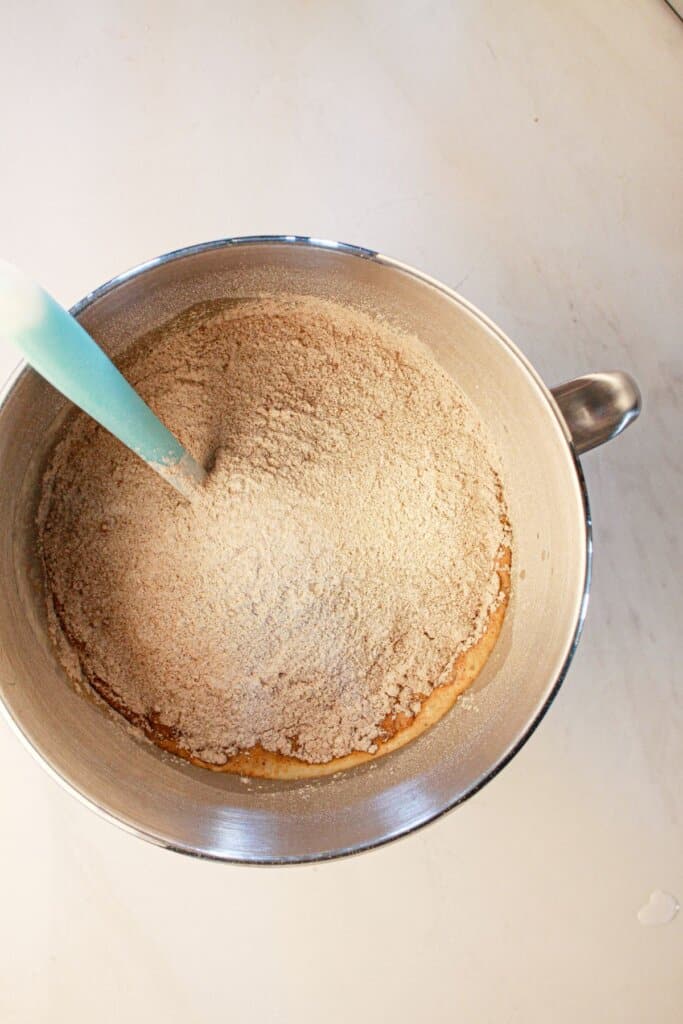 Flour being added to wet ingredients in a mixing bowl.