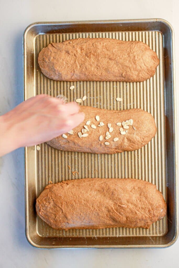 Oats being sprinkled on top of dough on a baking sheet.