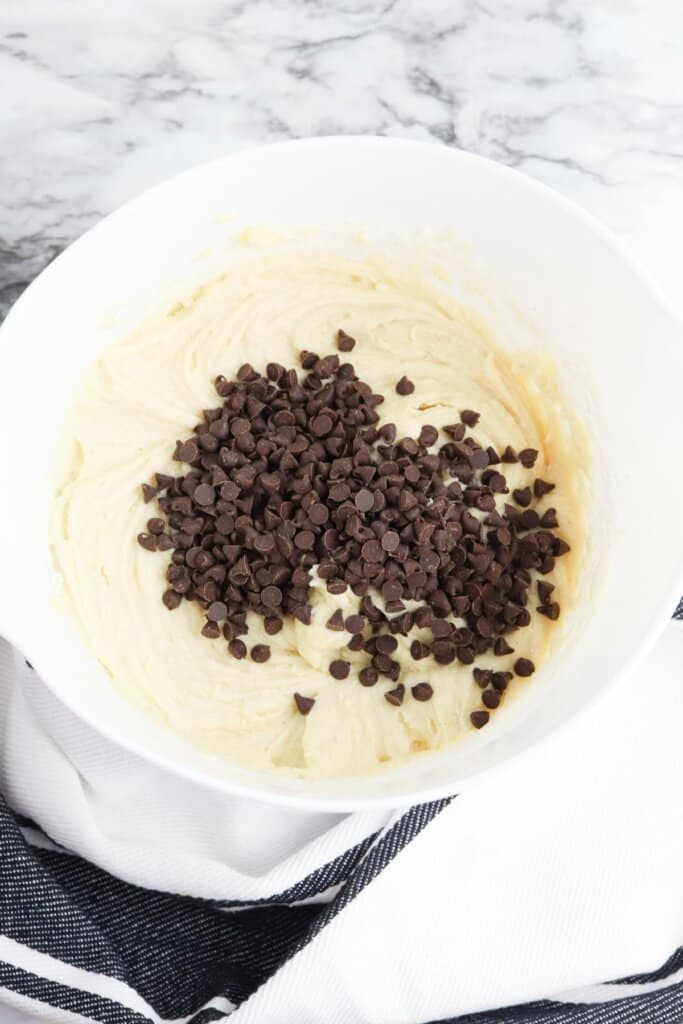 Chocolate chips being added to batter in a bowl.