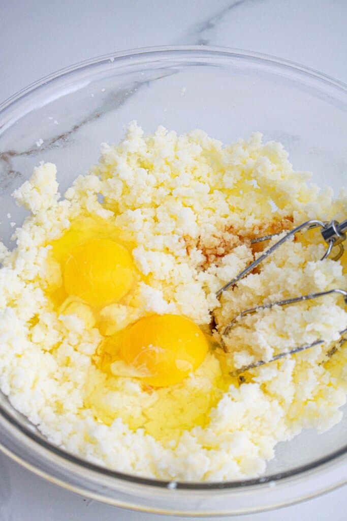 Eggs being mixed into butter and sugar in a glass bowl.