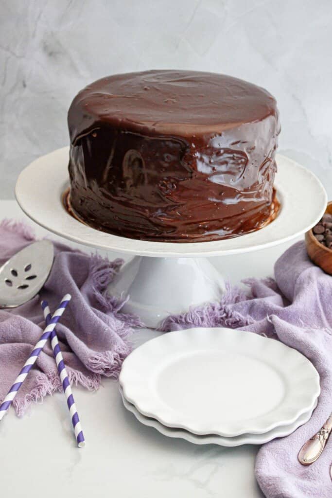 Chocolate ganache topped cake on a cake stand.