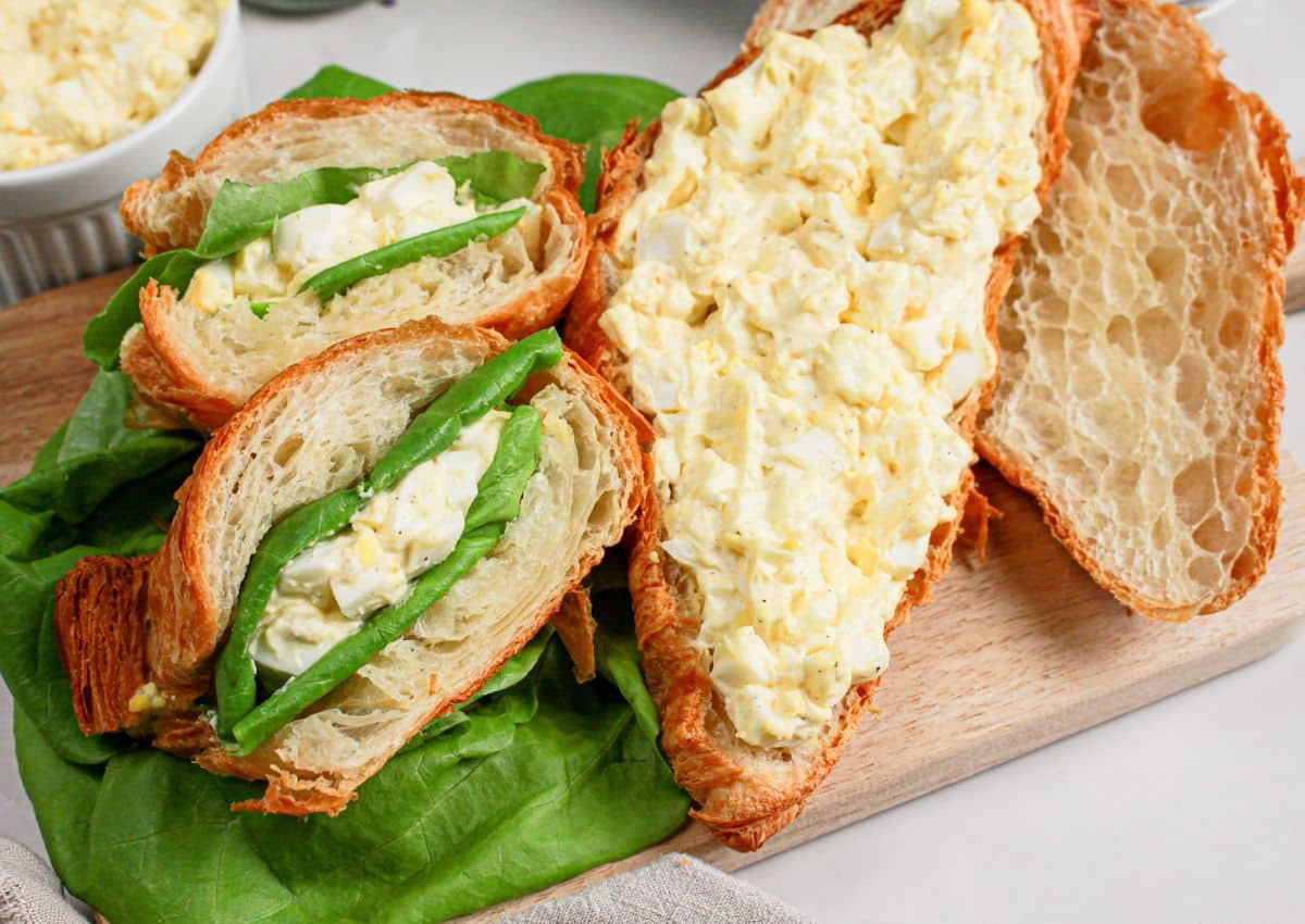 Egg salad sandwiches on a wooden cutting board.