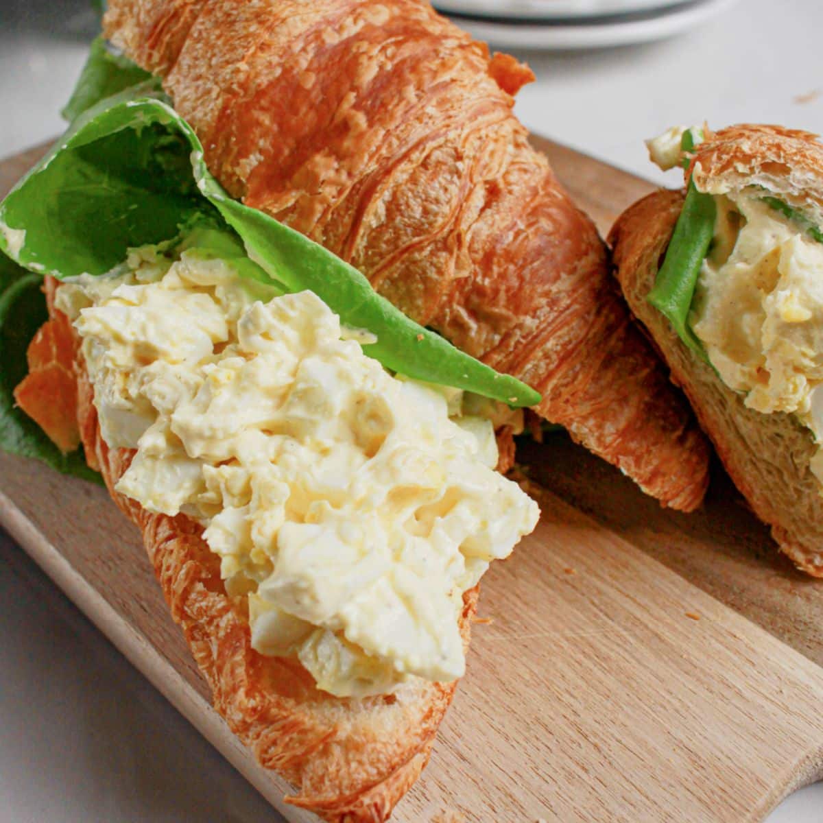 Egg salad sandwiches on a wooden cutting board.