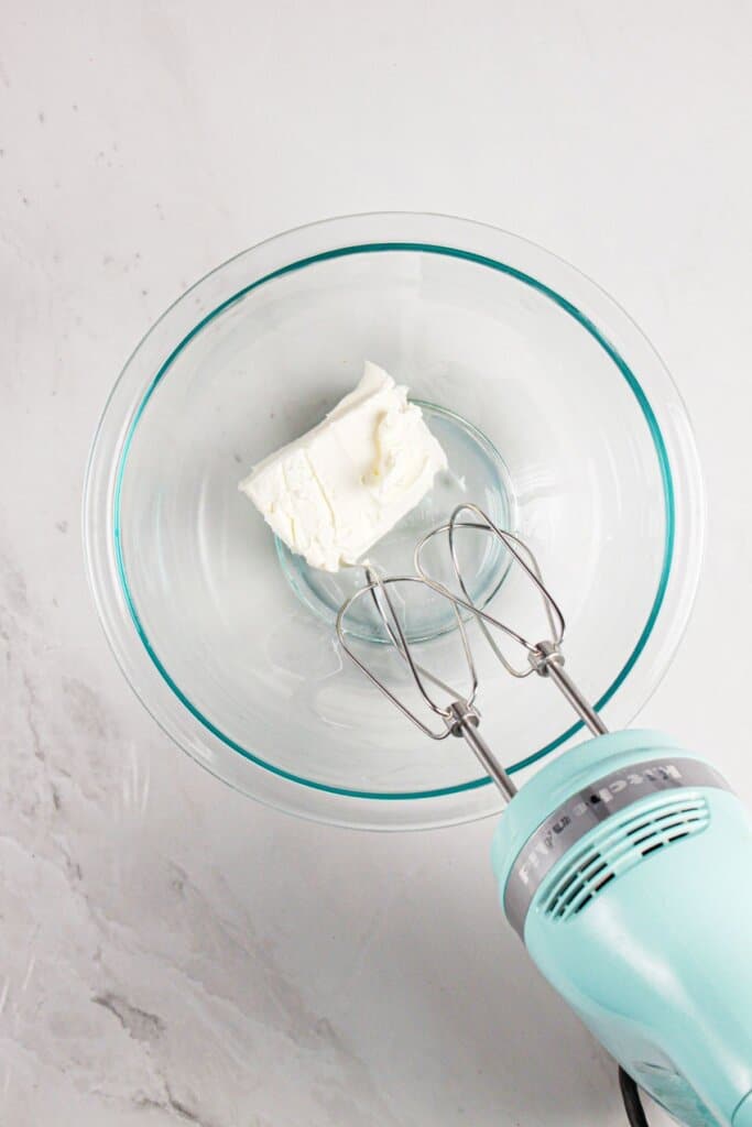 Cream cheese being mixed in a glass bowl.