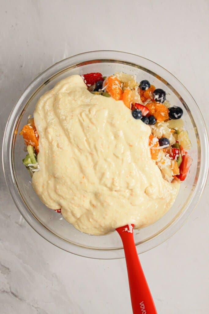 Pudding is being mixed with fruit in a glass bowl.