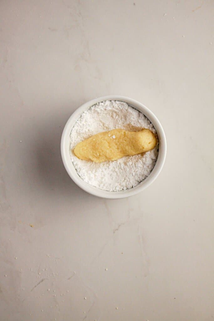 Dough log being rolled in powdered sugar.