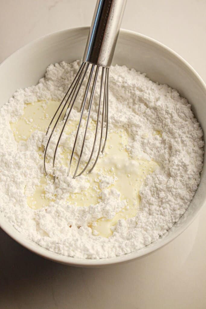Powdered sugar and cream being mixed in a bowl.