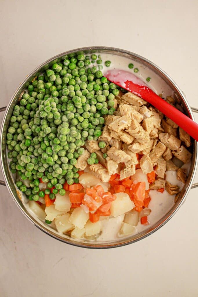 Veggies are being added to the creamy sauce in a pot.