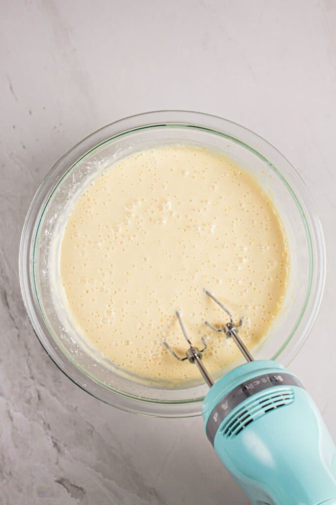 Batter being mixed with an electric mixer in a glass bowl.