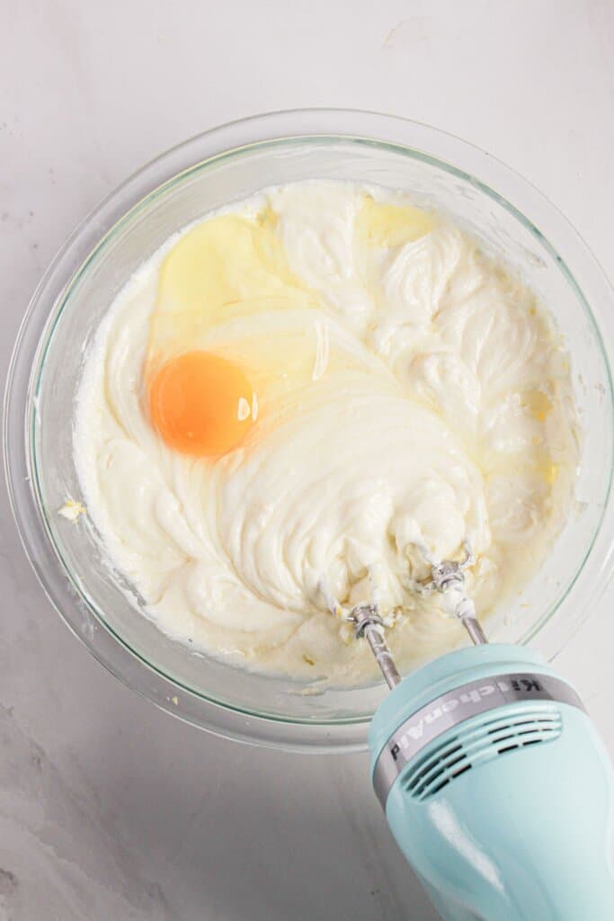 Eggs being mixed into batter in a glass bowl.