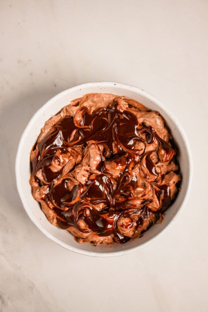 Hot fudge is being swirled into pudding in a bowl.