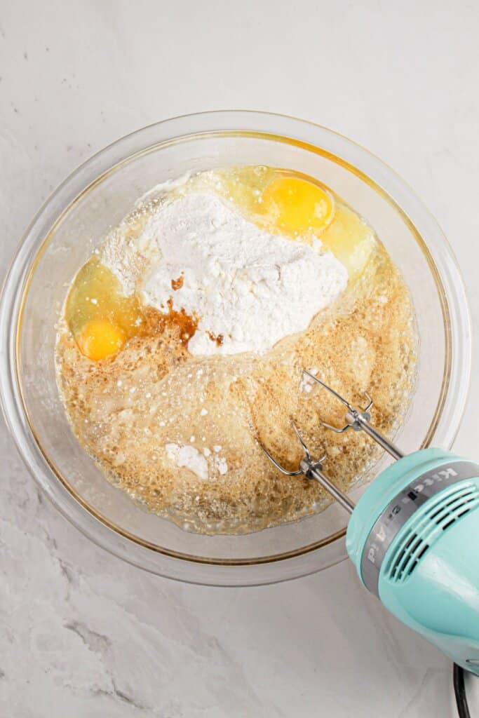 Cake batter is being mixed in a glass mixing bowl.