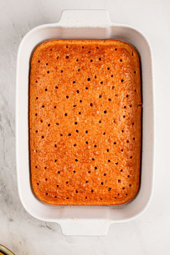 Holes being poked in a cake in a white baking dish.