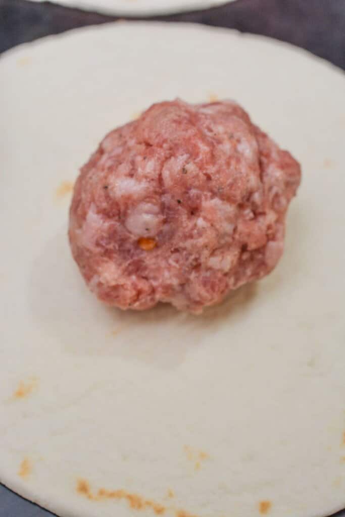 Sausage being pressed on a tortilla.