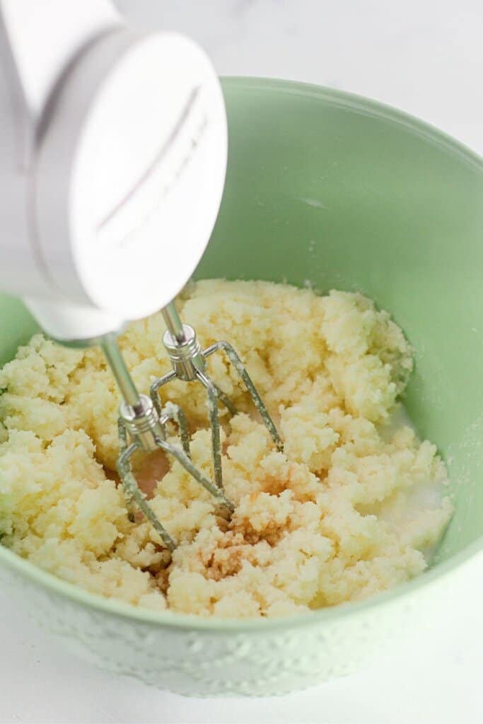 Butter and sugar being mixed in a green mixing bowl.