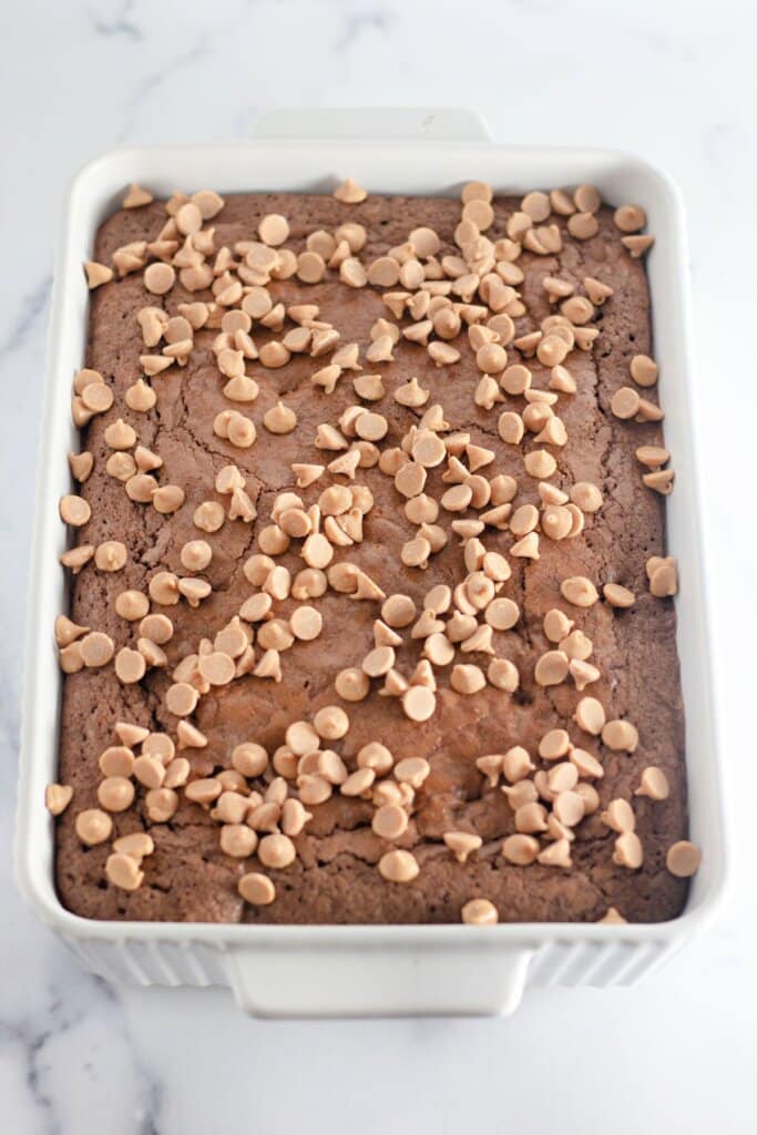 Peanut butter chips being sprinkled on top of dessert in a baking dish.