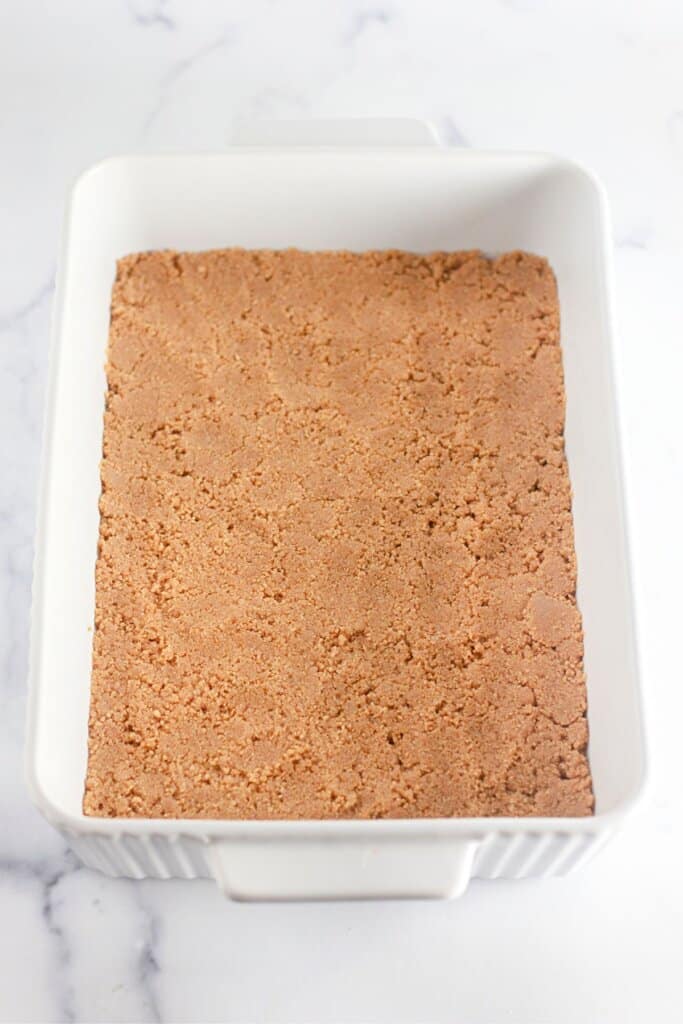 Crust being pressed into a white baking dish.