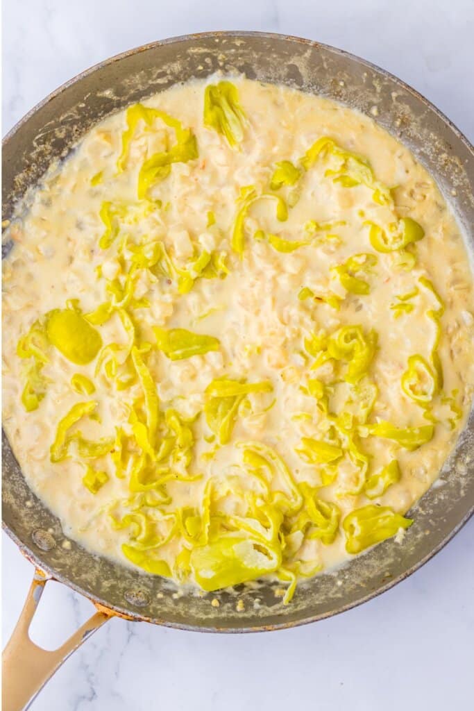 Peppers being added to a skillet with cream sauce,