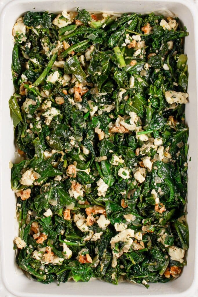 Spinach being added to baking dish.