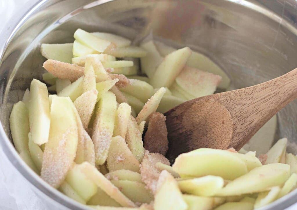 Apples being mixed with cinnamon and sugar in a bowl.