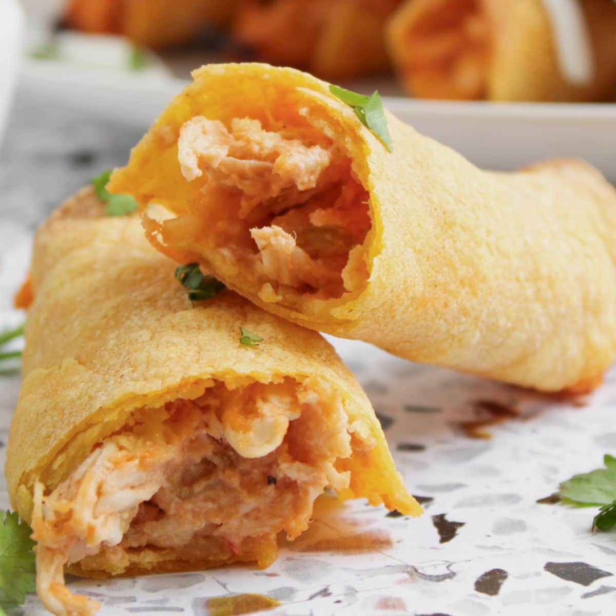 Chicken taquito broken in half on a plate.