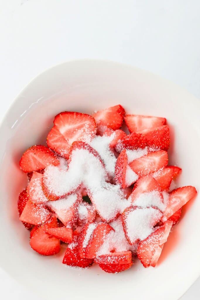 Strawberries and sugar being mixed in a bowl.