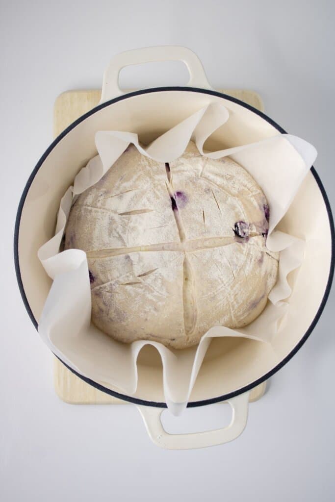 Scored loaf in a parchment lined pot.