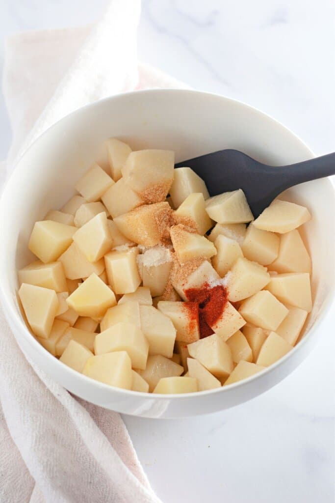 Potatoes being seasoned in a bowl.