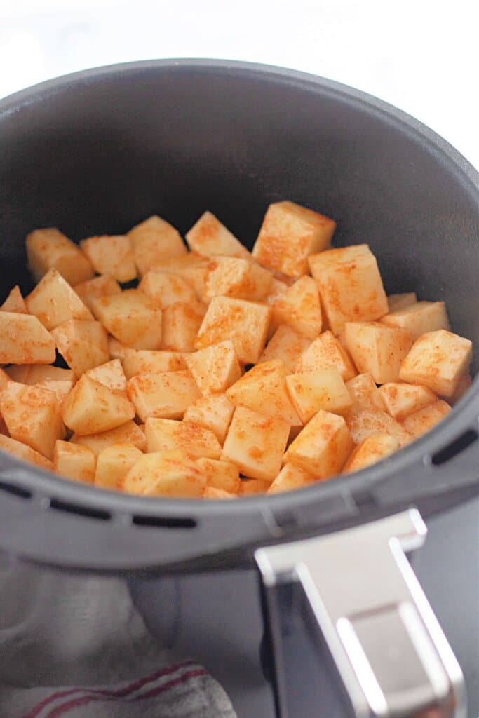 Seasoned potatoes in an air fryer basket.