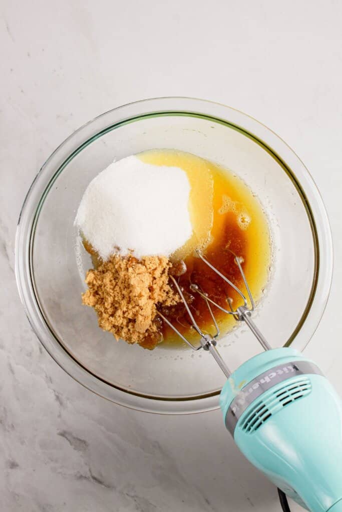 Sugar, butter, and vanilla being mixed in a glass bowl.