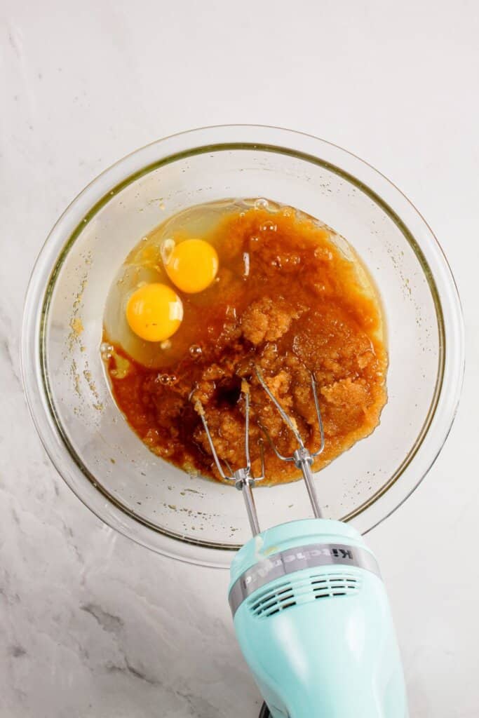 Eggs being added to wet ingredients in a mixing bowl.