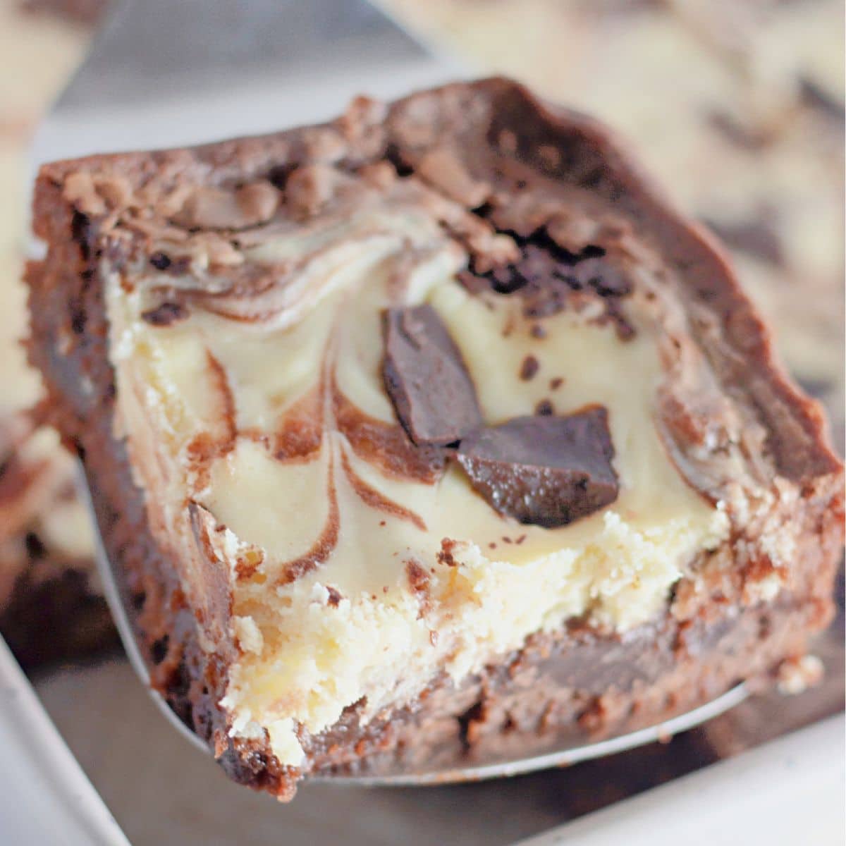 Slice of chocolate cheesecake brownies on a metal spatula.