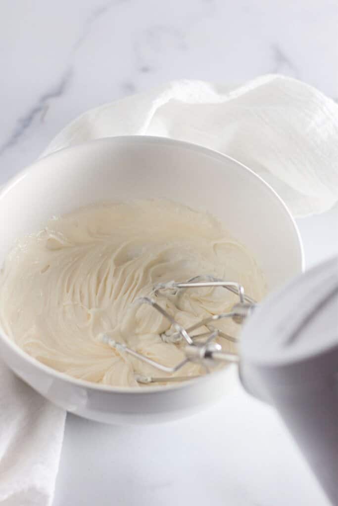 Cream cheese being mixed with a hand mixer.