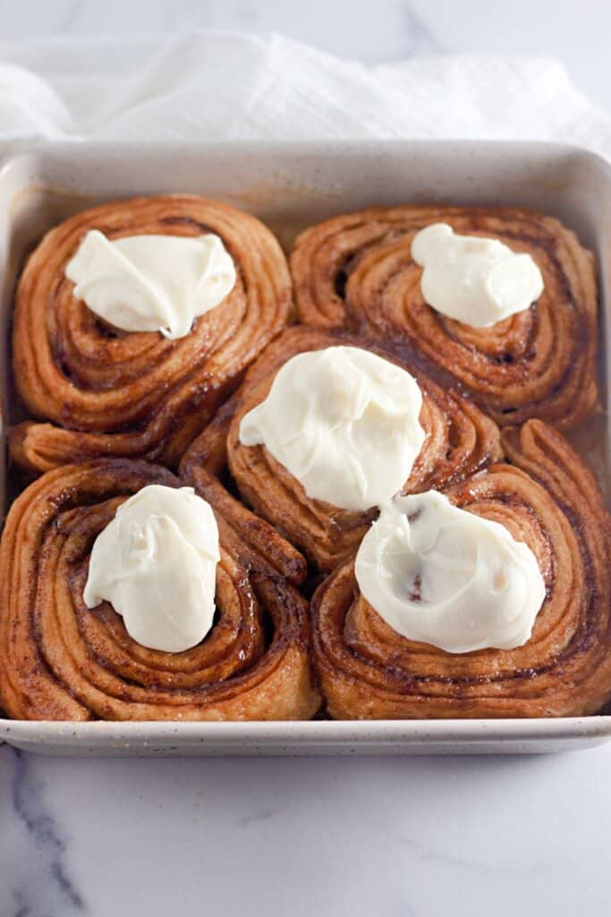Frosting being spread on cinnamon rolls in a baking dish.