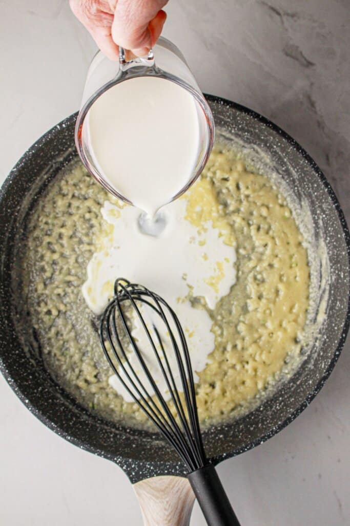 Cream being added to a skillet with a roux.
