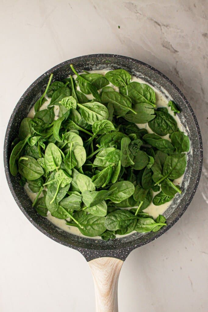 Spinach being added to a large skillet.