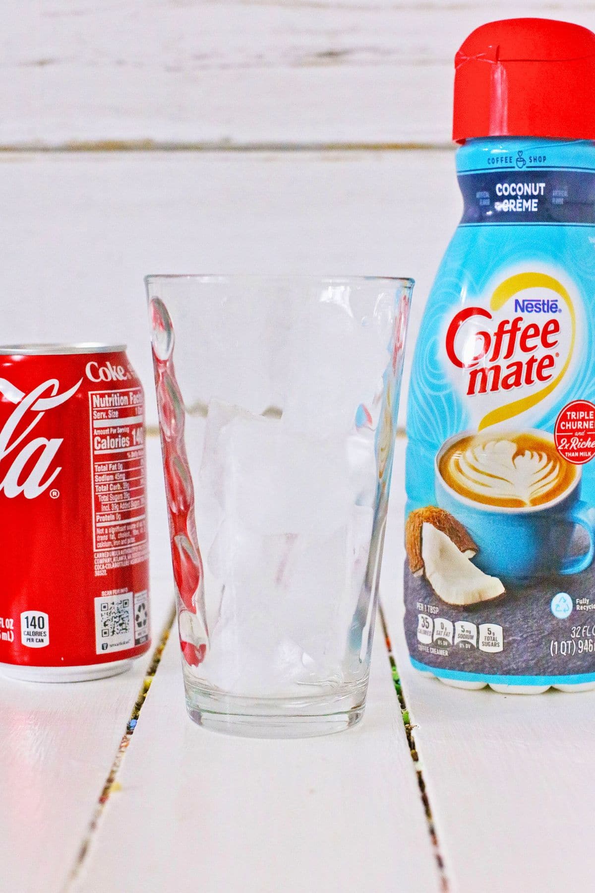 Glass, can of soda, and coffee creamer on a counter.