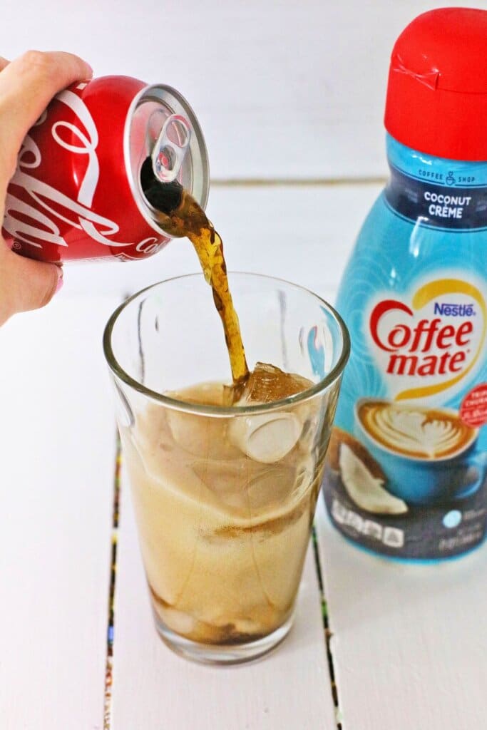 Soda being poured over ice in a glass.