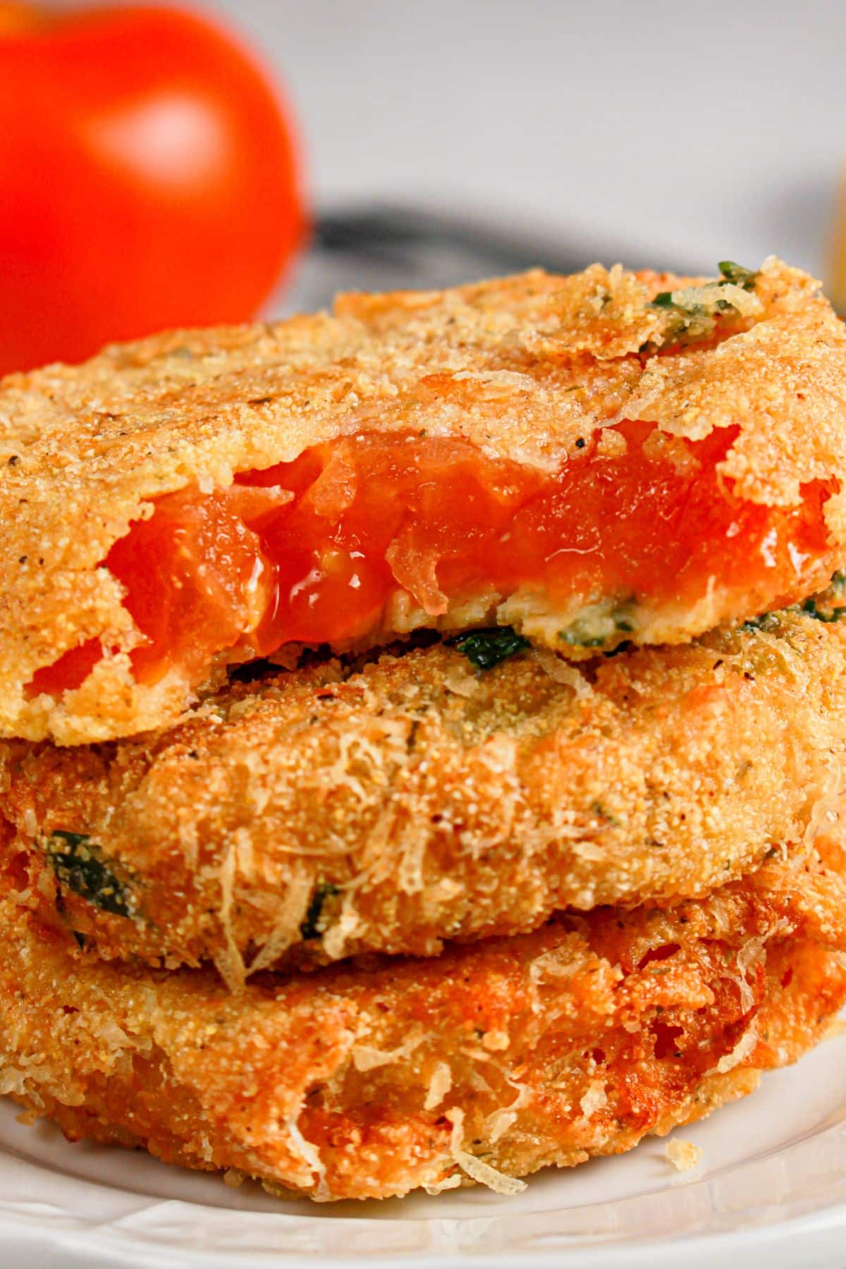 Three slices of fried red tomatoes stacked on a plate.