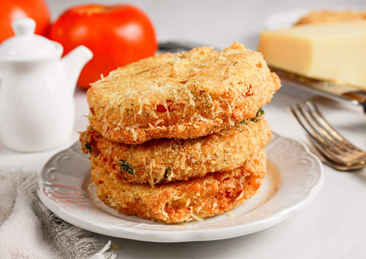Three slices of fried red tomatoes stacked on a plate.