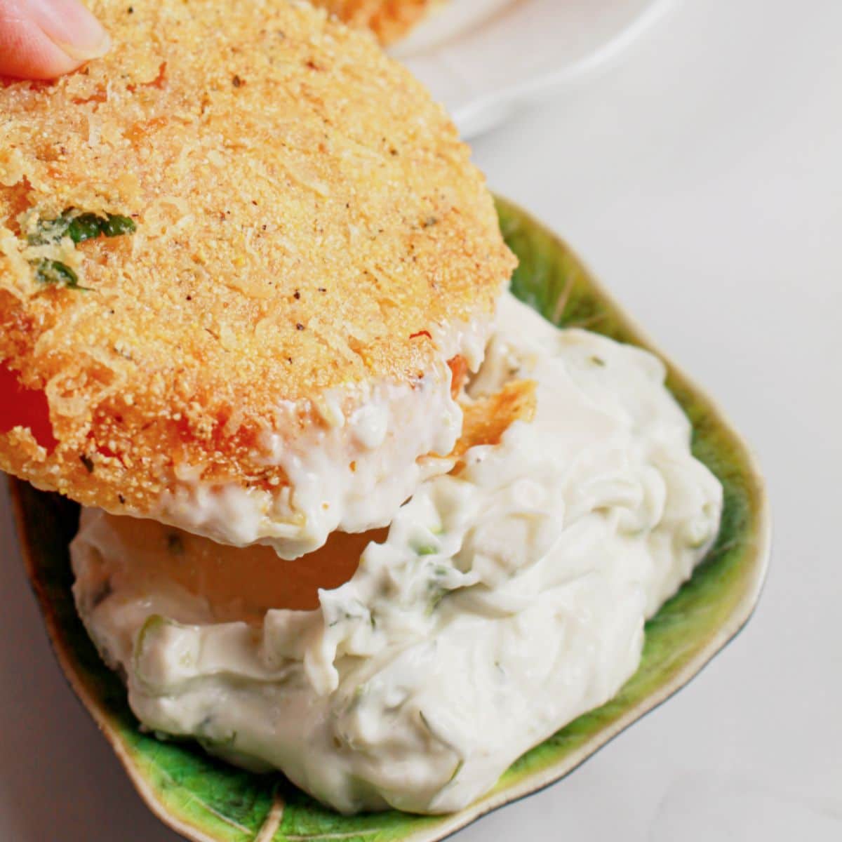 Tomato being dipped into a bowl of dipping sauce.