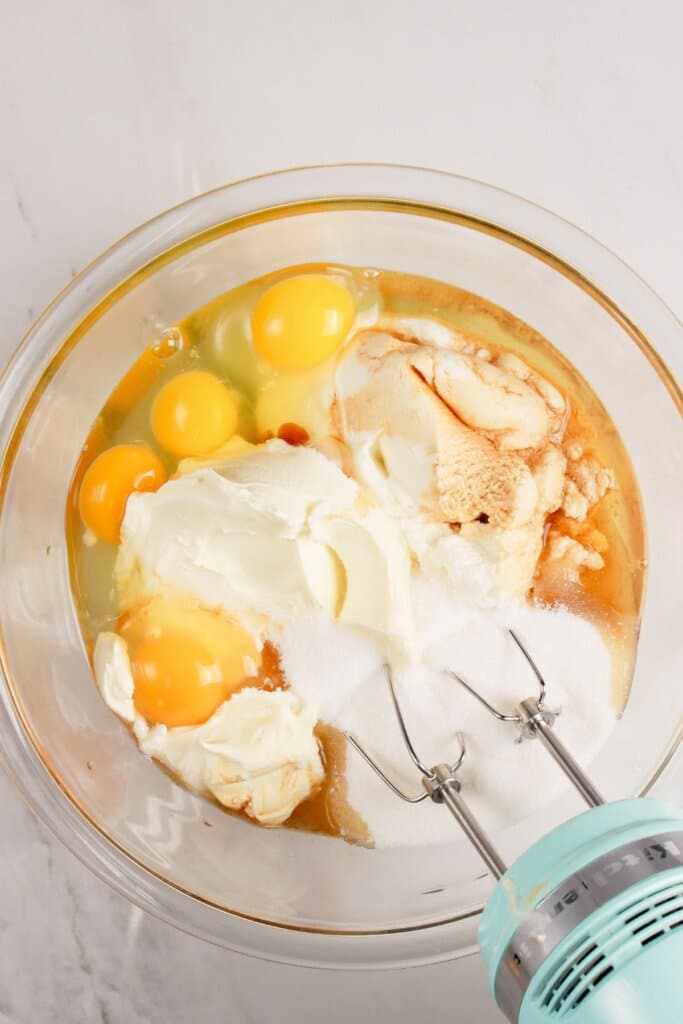 Eggs and cheese are being mixed in a glass bowl.